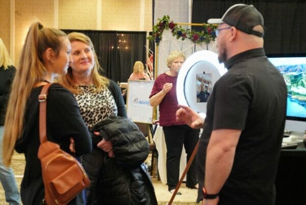 Brides to Be and mom speaking with exhibitor at wedding show.